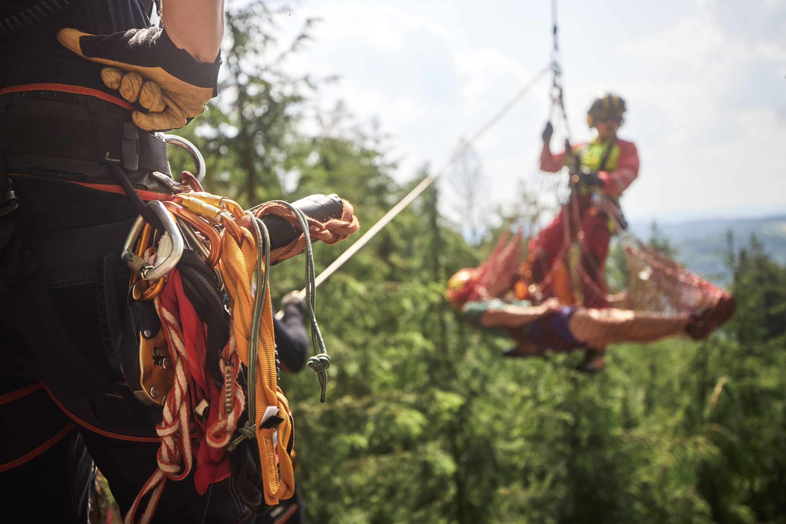 Paramedic with patient in stretcher under helicopter. Teams of emergency medical service and firefighters training rescue injured person from inaccessible terrain. Selective focus on safety harness.