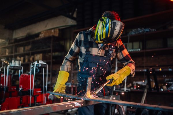 Skilled welder assembling durable pipelines for infrastructure projects while using his welding machine with great responsibility.Focus on yellow sparks coming out while he is welding a piece of metal